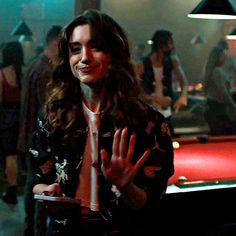 a woman standing in front of a pool table holding her hand up to the camera