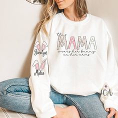 Custom Easter Mama Sweatshirt With Kids Names, This Mama Wears Her Bunnies On Her Arms Crewneck Sweatshirt, Mama Easter Sweatshirt Processing Time is 2 weeks. Processing time does not include shipping which is an additional 3-5 business days. Upgrade shipping options available at check out. This shirt is unisex cotton/polyester blend crewneck sweatshirt. All styles are super soft. Shirt sizes range from Adult S to 3XL. Size availability will vary. If the size you choose is out of stock with our White Long Sleeve T-shirt With Lettering, Spring Long Sleeve Tops With Lettering, Long Sleeve Tops With Letter Print For Mother's Day, Long Sleeve Tops For Mother's Day Loungewear, White Cotton Sweatshirt For Mother's Day, Crew Neck Tops With Name Print For Loungewear, White Tops With Lettering For Mother's Day, White Long Sleeve Sweater With Name Print, Crew Neck Top For Mother's Day Loungewear