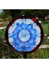 a blue and white glass flower on top of a metal pole in the middle of some grass