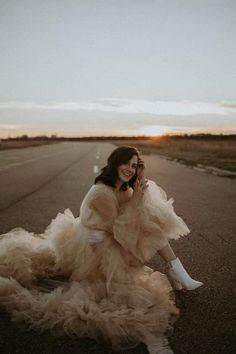 a woman is sitting on the side of an empty road talking on her cell phone