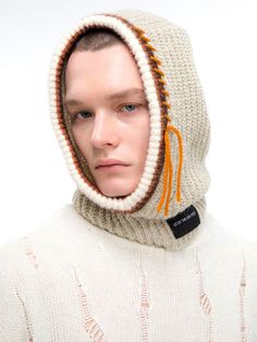 a man wearing a knitted hoodie with orange tassels on his head