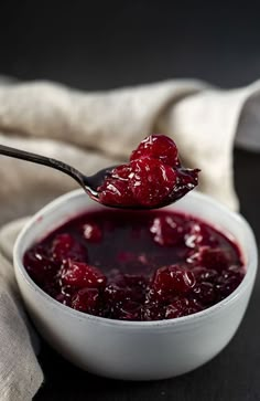 a spoon full of cranberry sauce on top of a white bowl next to a napkin