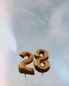 two gold balloons shaped like the number twenty eight are floating in the air against a cloudy blue sky