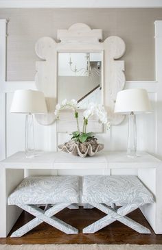 a white table with two lamps and a mirror on it's wall next to a bench