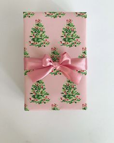 a present wrapped in pink wrapping paper with christmas trees on it and a pink bow