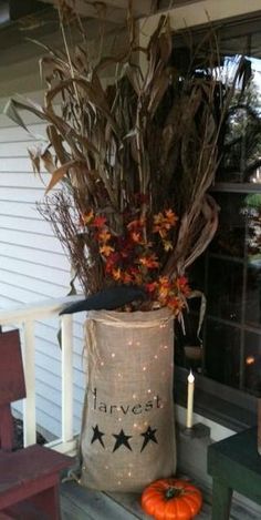 a bag filled with leaves sitting on top of a porch next to a candle and some pumpkins