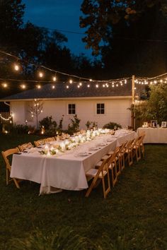 a long table is set up outside with candles and lights strung over it for an outdoor dinner