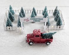 a red truck with a christmas tree on the back is parked in front of a white picket fence