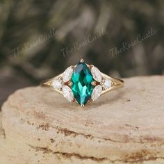 an emerald colored ring with white diamonds on top of a stone slab in front of some rocks