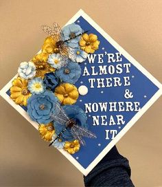 a blue and gold graduation cap with flowers on it that says, we're almost there & nowhere near it