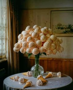 a vase filled with flowers sitting on top of a table next to small cones and seashells