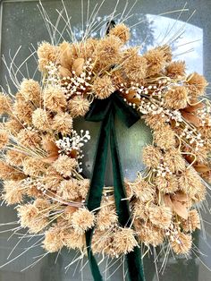 a wreath is hanging on the front door with green ribbon and white flowers in it