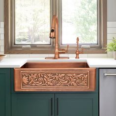 a copper sink in a kitchen with green cabinets and white counter tops next to a window