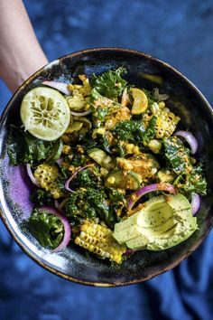 a person holding a bowl filled with vegetables and avocado on top of it