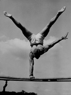 a man doing a handstand on top of a high bar with one leg in the air