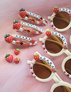 several pairs of sunglasses with strawberries and name tags attached to them on a pink surface