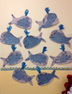 a group of paper cut out of blue fish on a white wall next to a teddy bear