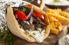 a pita filled with meat and vegetables on top of a wooden cutting board next to fries