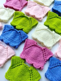 many knitted pieces of clothing are arranged on a white surface, including pink, green and blue