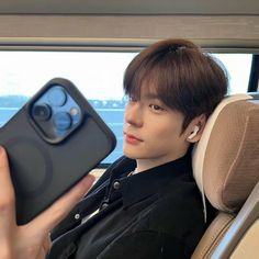 a young man sitting in a car holding up an iphone case with ear buds on it