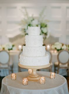 a white wedding cake sitting on top of a table next to candles and flower centerpieces