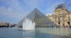 a large glass pyramid in the middle of a fountain with people standing around it and buildings behind it