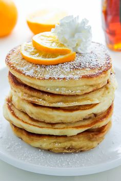 a stack of pancakes topped with powdered sugar and orange slices