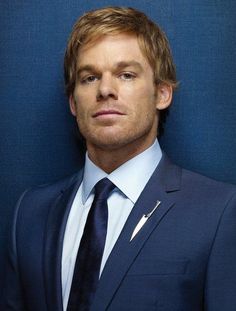 a man in a suit and tie poses for a photo against a blue background with his head tilted to the side