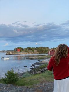 a woman is flying a kite near the water and boats on the shore in the distance