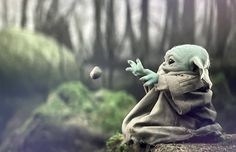 a baby yoda doll sitting on top of a moss covered rock in the woods