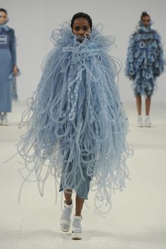 a woman is walking down the runway wearing a blue dress with large feathers on it