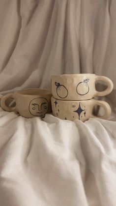 three ceramic bowls sitting on top of a white cloth covered tablecloth with fruit drawn on them