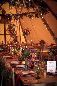 a table set up with place settings and flowers in front of a tented area