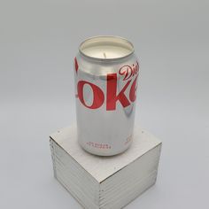 a can of diet coke sitting on top of a stack of books with a lit candle in the middle