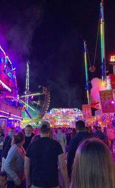 people are walking around an amusement park at night with lights and rides on the sides