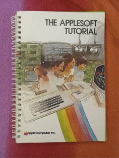 the apple book is open to show people working on computers and other electronic equipment in front of them