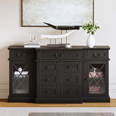 a black sideboard with glass doors and drawers in front of a painting on the wall