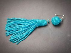 the beaded tasselle is hanging from a hook on a gray surface with silver earwires