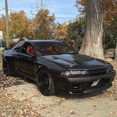 a black car parked in front of a tree with leaves on the ground next to it