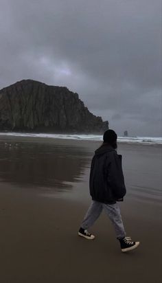 a person walking on the beach in front of an island with a large rock sticking out of it