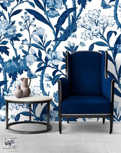 a blue chair sitting next to a table with vases on top of it in front of a floral wallpaper