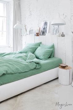 a bed with green sheets and pillows in a white room next to a table lamp