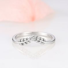 a white gold ring with two leaves on the side and a pink flower in the background