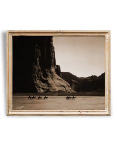 black and white photograph of people riding horses through the desert with mountains in the background