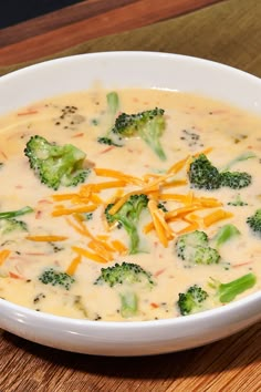 a white bowl filled with broccoli cheese soup on top of a wooden table