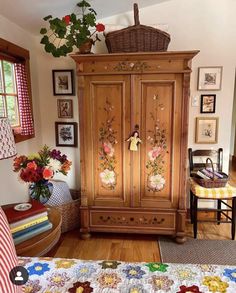 a wooden armoire in a room with pictures on the wall and flowers hanging above it