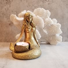 a gold mermaid candle holder sitting on top of a table next to a white flower