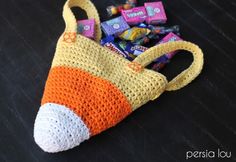 an orange and white crocheted bag with candy in it on a table next to some candies