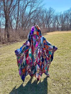 a woman is standing in the grass wearing a colorful dress with an open hood and long sleeves