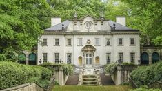 an old white house surrounded by trees and bushes with stairs leading up to the front door